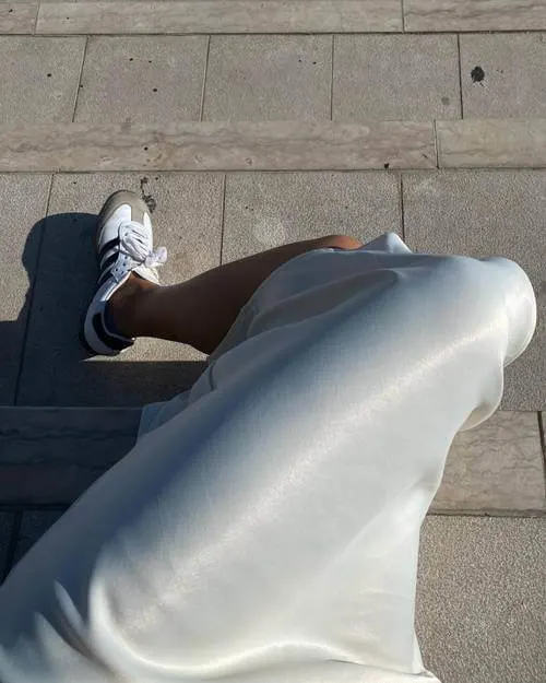 a woman wearing silky long dress and white Adidas Samba sneakers