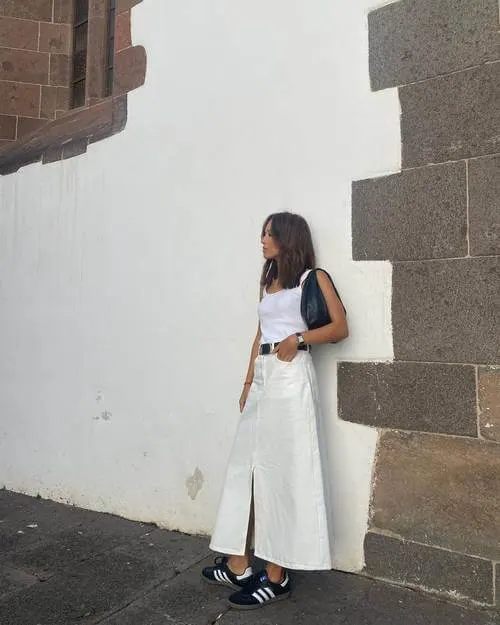 a woman wearing white tank top, white maxi skirt, and black Adidas Samba sneakers