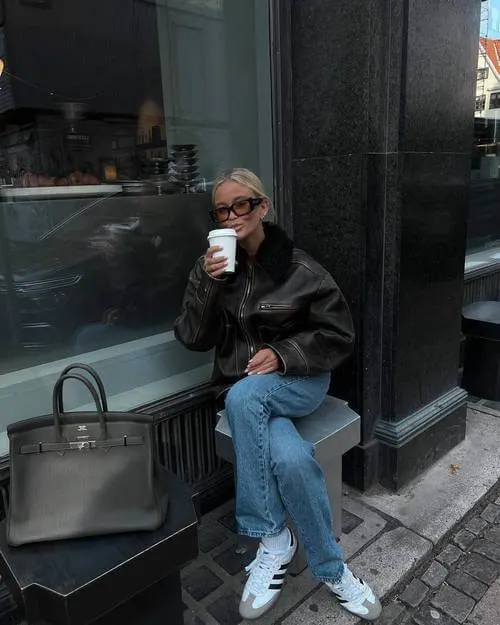 a woman wearing black leather jacket, blue straight leg jeans, and white Adidas Samba sneakers