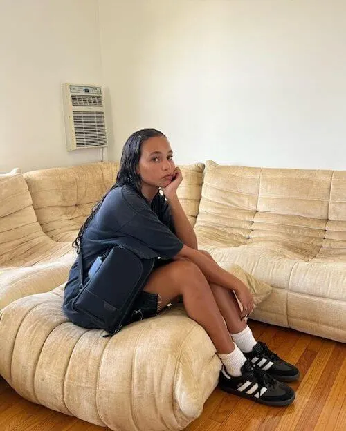 a black girl wearing navy blue oversized tshirt, denim mini skirt, and black Adidas Samba sneakers