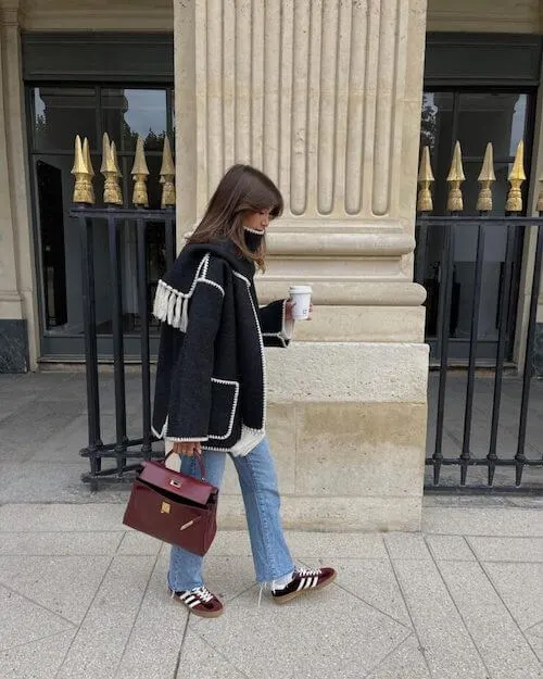 a woman wearing black short coat, blue jeans, and Adidas Samba sneakers