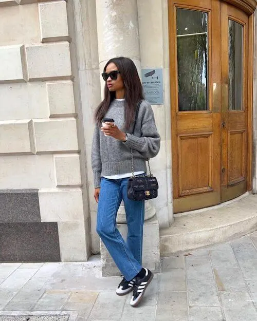 a black woman wearing black Adidas Samba sneakers, gray sweater, and blue jeans