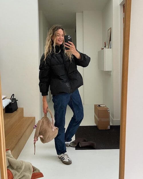 a woman wearing white Adidas Samba sneakers, black puffer jacket, dark blue jeans