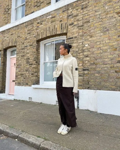 a woman wearing beige sweater, brown pants, and white Adidas Samba sneakers