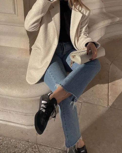 a woman wearing cream oversized blazer, blue jeans, and black Adidas Samba sneakers