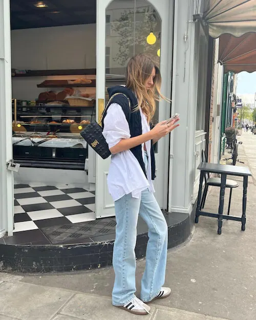 a woman wearing white button down shirt, light blue wash jeans, and white Adidas Samba sneakers