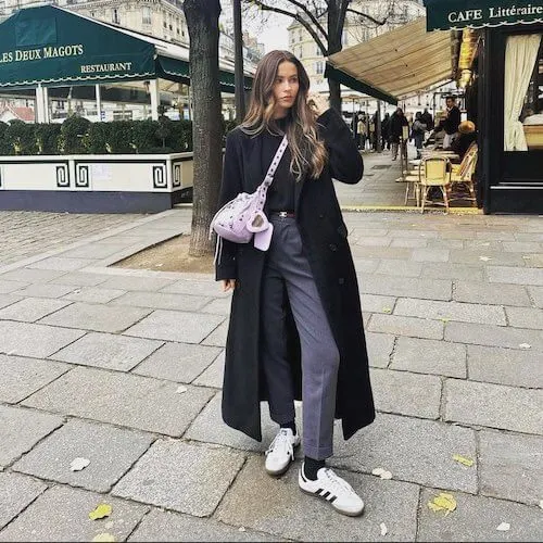 a woman wearing white Adidas Samba sneakers, black coat, and gray pants