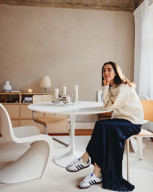 a woman wearing a pair of white Adidas Samba sneakers, an oversized chunky knit sweater, and a black maxi dress