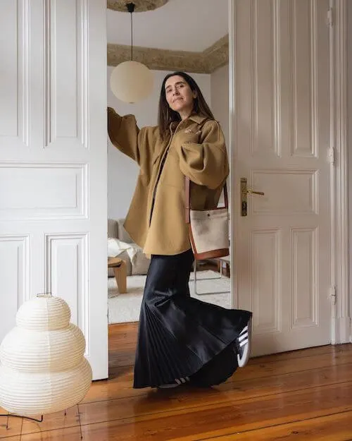 a woman wearing beige oversized shirt, black maxi dress, and black Adidas Samba sneakers