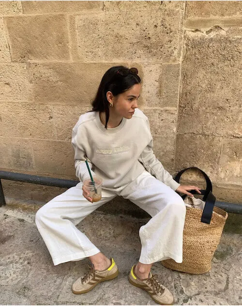 a woman wearing beige sweatshirt, white pants, and tan Adidas Samba sneakers