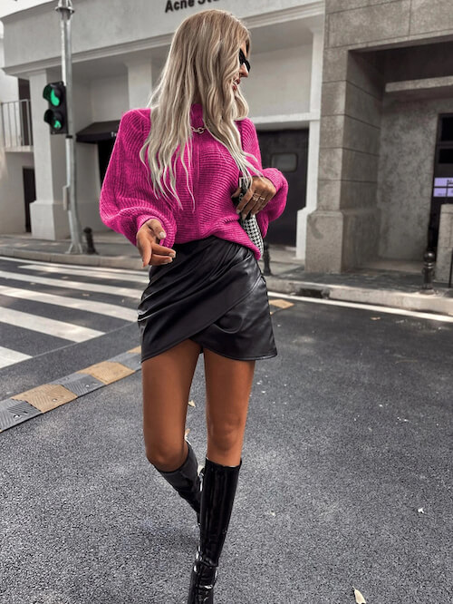 a woman walking around Vegas during the day, wearing a hot pink sweater, a black leather skirt, and a pair of black knee high boots