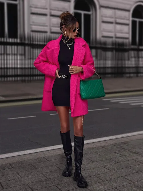 a woman on Las Vegas street, wearing a hot pink coat, a black knit dress, a belt, a green handbag, and a pair of black boots