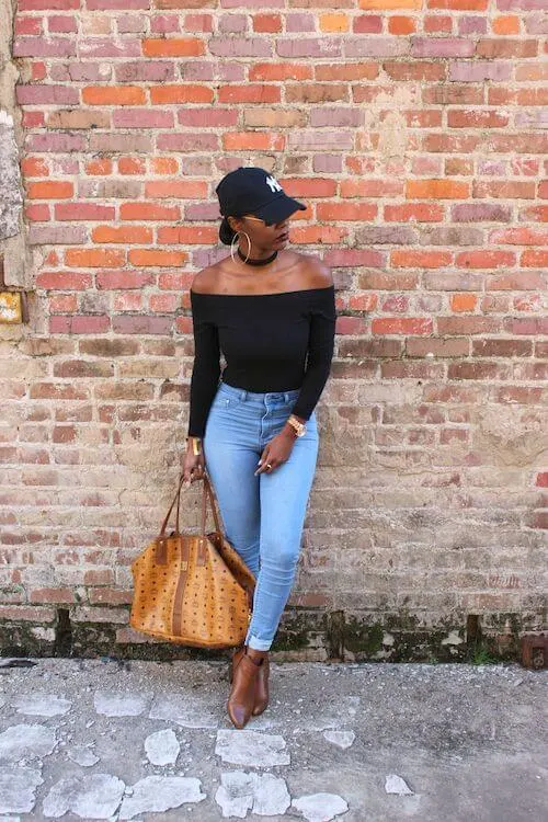 a black woman wearing a baseball hat, an off shoulder shirt, and blue jeans