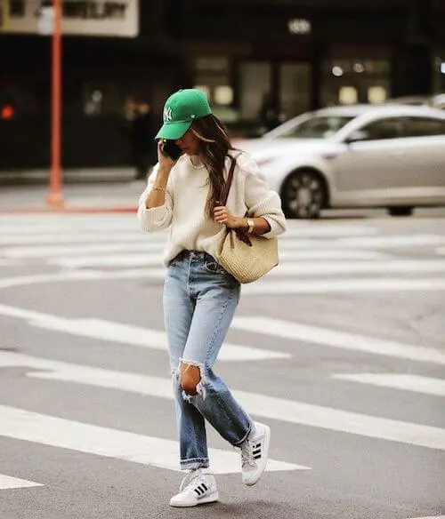 a woman wearing green baseball cap, oversized sweater, and jeans