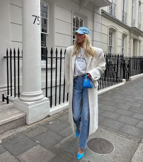 a woman wearing blue baseball hat, long coat, and jeans