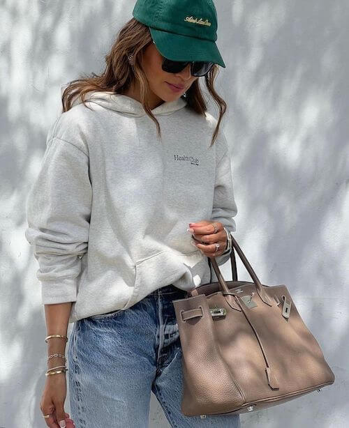 a woman wearing green baseball hat, hoodie, and jeans