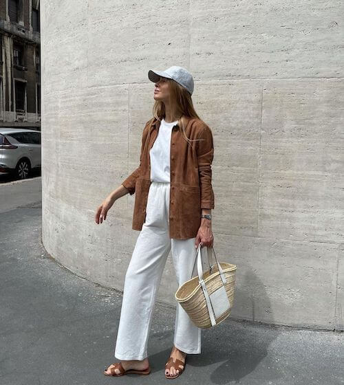 a woman wearing a white baseball hat, tan button down shirt, and white wide leg pants