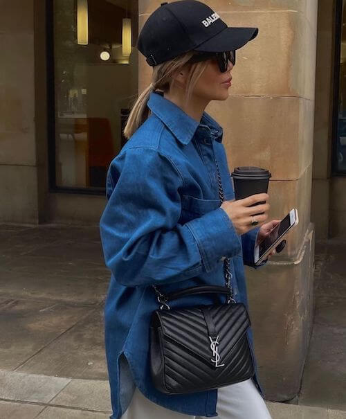 a woman wearing denim shirt, baseball hat, and black bag