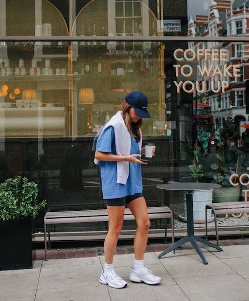 a woman wearing a baseball hat, blue oversized Tee, biker shorts, and white sneakers