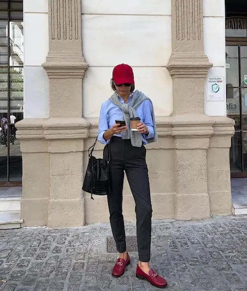 a woman wearing a red baseball hat, blue shirt, black pants and red loafers