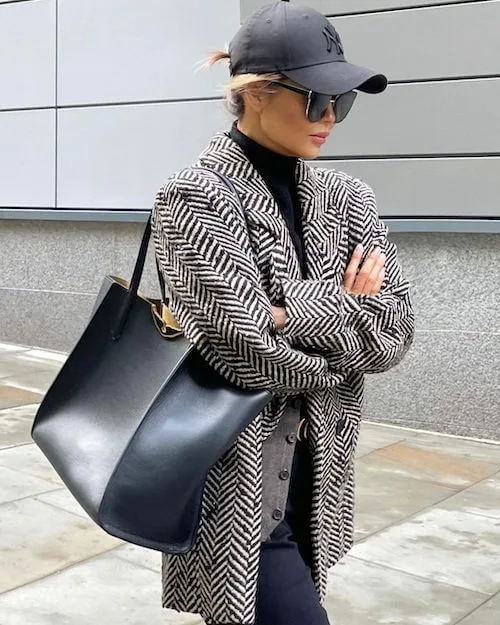 a woman wearing a black baseball hat, winter blazer, and black tote