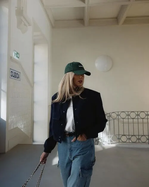 a woman wearing a baseball hat, black jacket and jeans