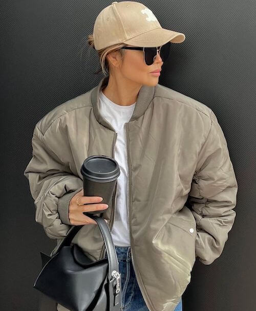 a woman wearing a beige baseball hat, and beige bomber jacket