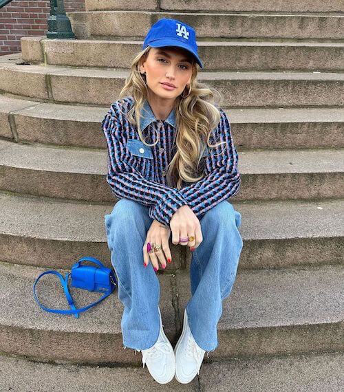 a woman wearing a blue baseball hat, blue striped shirt, and jeans