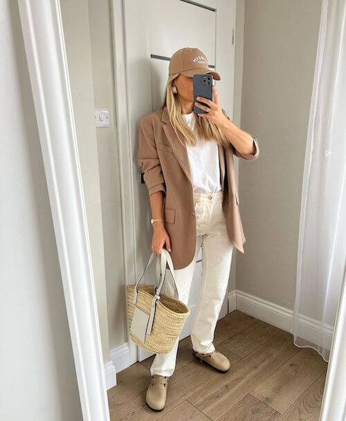 a woman wearing baseball hat, beige blazer and white jeans