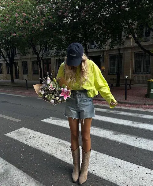 a woman wearing baseball hat, button down, and denim shorts