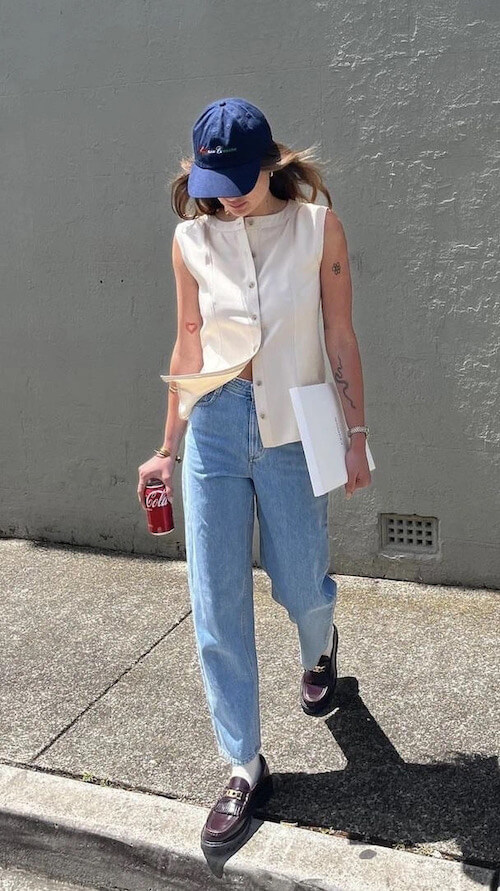 a woman wearing a baseball hat with white sleeveless top and jeans