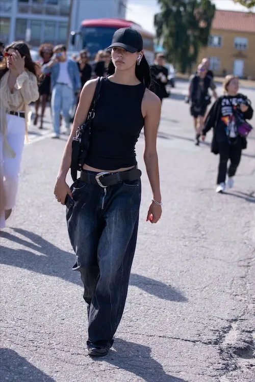 a woman wearing black baseball cap, black tank top, and baggy jeans