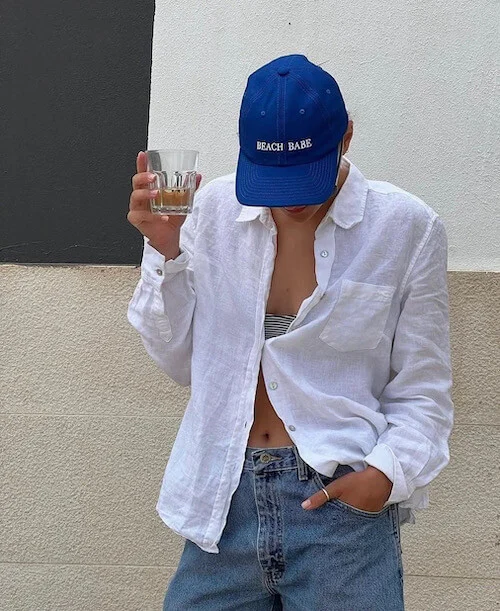 a woman wearing a blue baseball hat, white button down, and jeans
