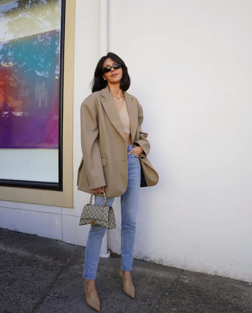 a woman wearing a beige blazer and blue jeans