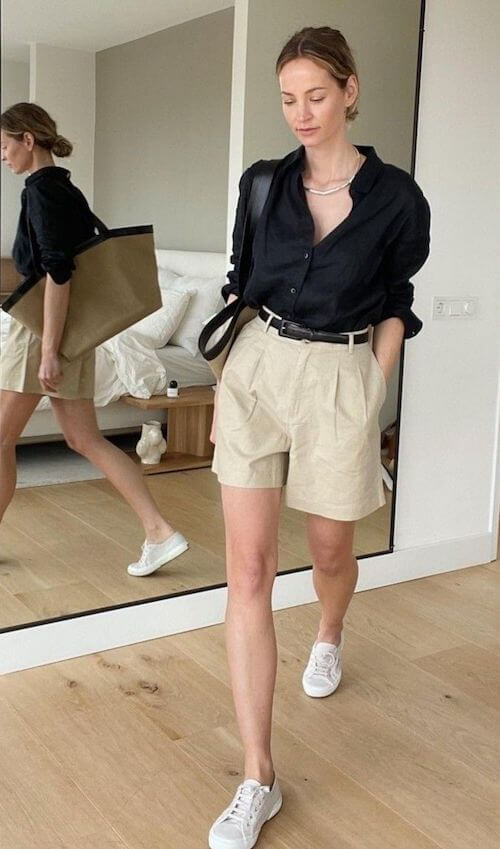 a woman wearing a black blouse, beige shorts, and white sneakers