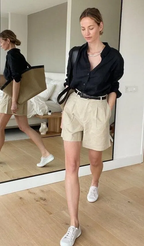 a woman wearing a black blouse, beige shorts, and white sneakers