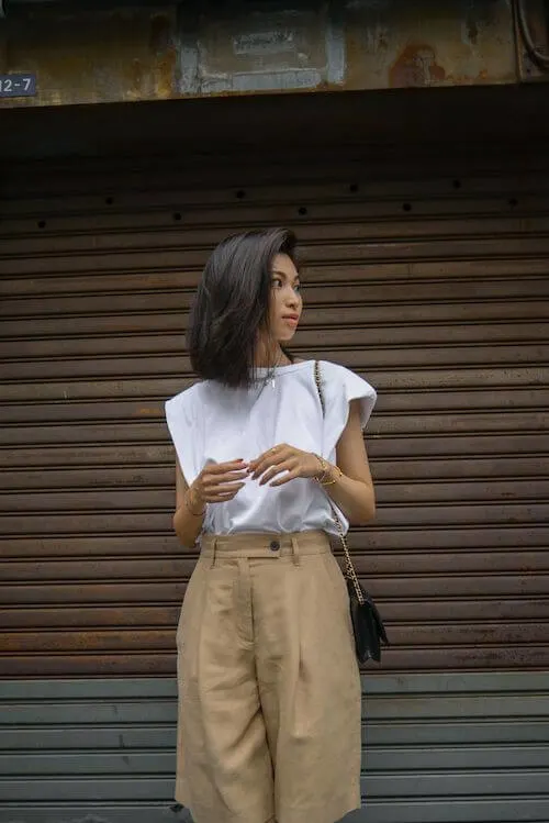 a woman wearing white padded shoulder shirt, and beige Bermuda shorts