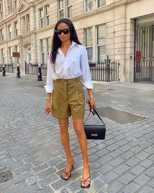 a black woman wearing a white shirt, beige shorts, flip flops, and sunglasses
