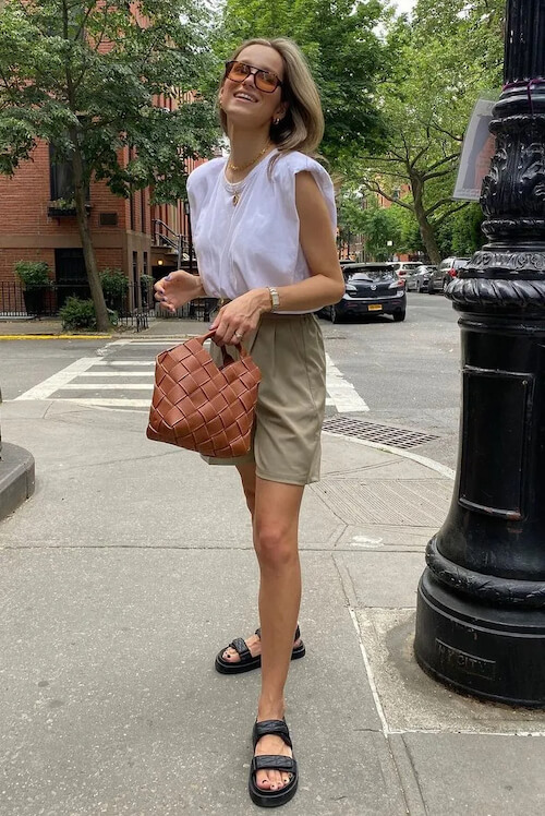 a woman wearing a white sleeveless top, beige shorts, and black sandals