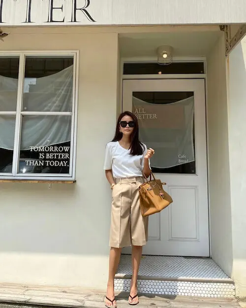 a woman wearing a simple white tee and beige Bermuda shorts