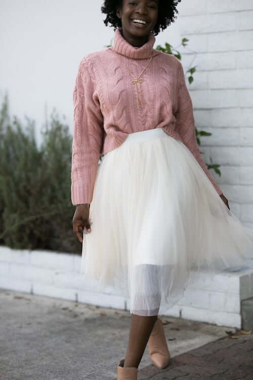 a black woman wearing a cute pink sweater, a white tulle skirt, and a pair of tan booties