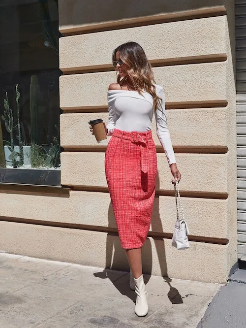 a woman wearing a long sleeve white shirt, pink midi skirt, a pair of white ankle boots