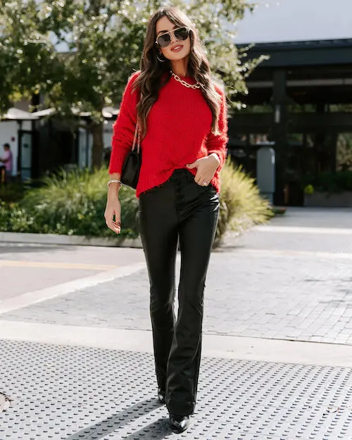 a woman wearing a red sweater, blakc flare pants, black boots, sunglasses, and a gold chain necklace