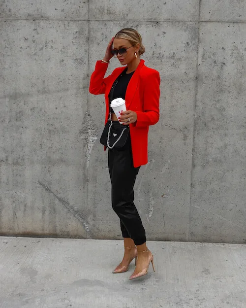 a woman wearing a black crop top, black joggers, heels, and a red blazer