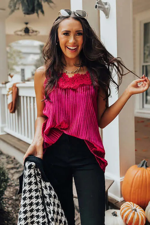 a woman wearing a pink cami top, black skinny jeans, and holding a black and white coat