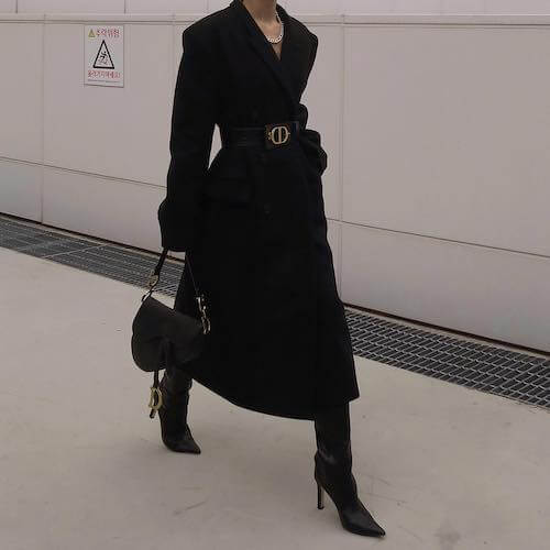 a woman wearing a long black coat with a belt