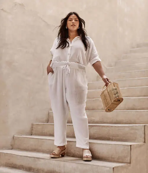 a plus size woman wearing a button down blouse and white pants set