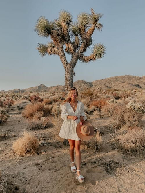 a cute young woman wearing white dress, white sandals, holding a straw hat