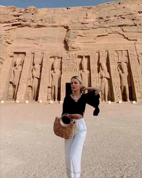 woman wearing black top, white pants and straw bag