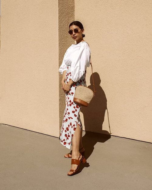 woman wearing silk blouse, floral midi skirt, sandals, and straw bag